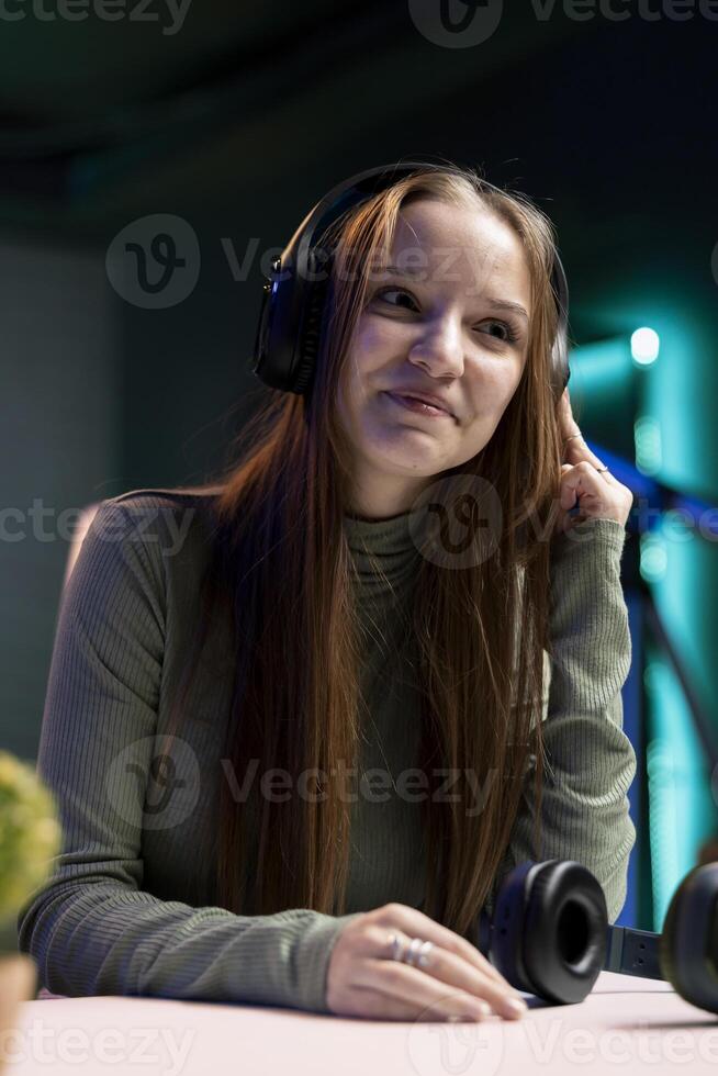 Smiling gen Z girl filming herself enjoying new album from favorite musician, reviewing music. Upbeat content creator hosts internet show, rating songs, hearing them through headphones photo