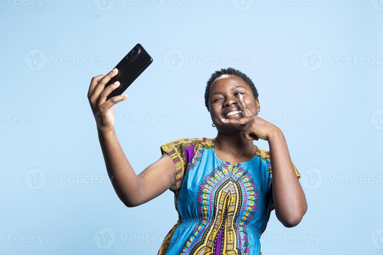 Positive joyful person taking photos on mobile phone app, showing her happiness and beautiful smile on social media platforms. African american model takes pictures on smartphone, cheerful girl.