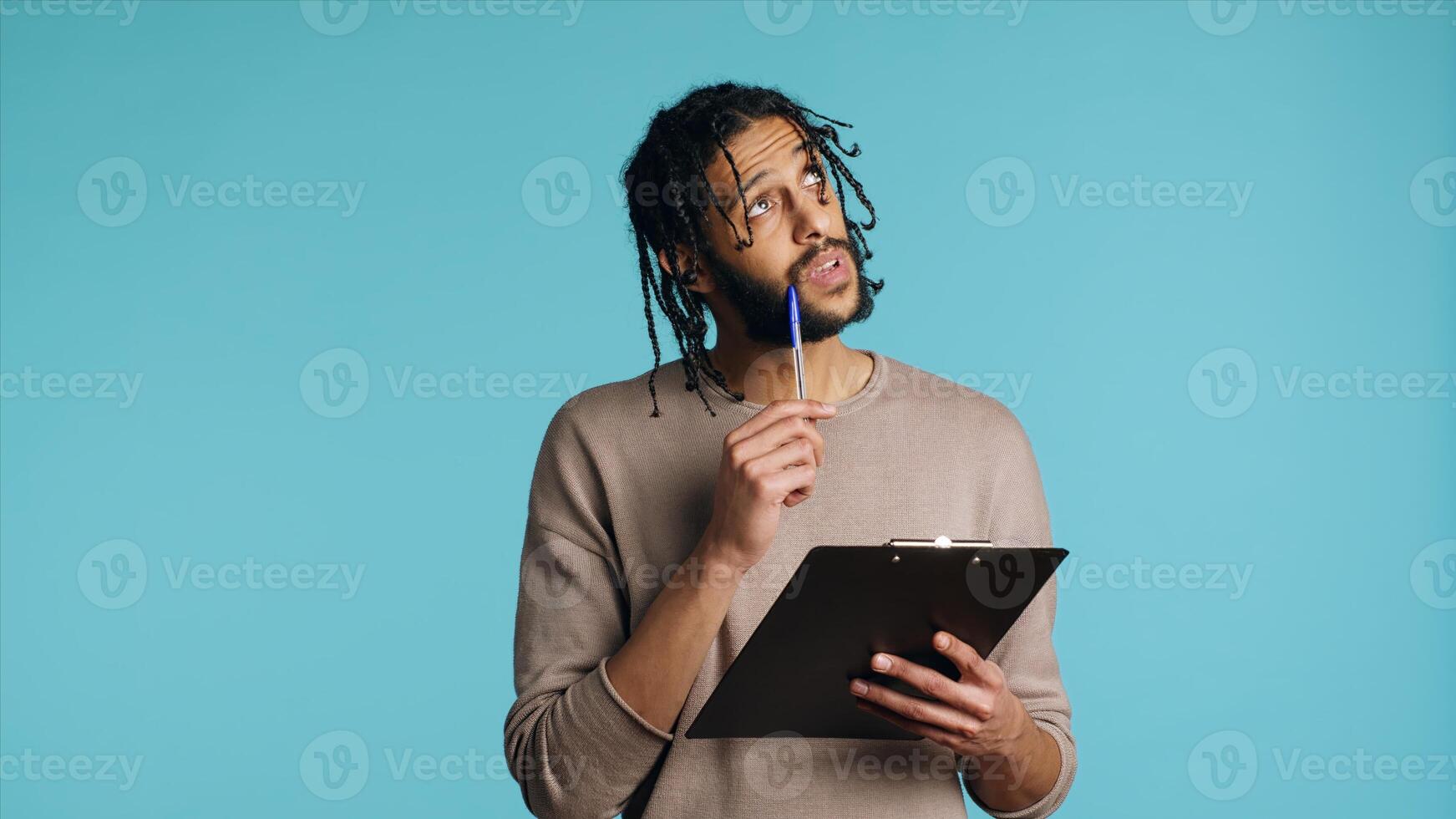 Creative man brainstorming ideas, writing on document using pen. BIPOC photographer using clipboard to complete shoot list for upcoming photography work, isolated over studio background, camera A photo