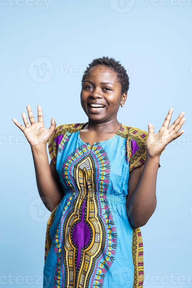 African american young adult feeling joyful over blue background, wearing authentic colorful attire on camera. Young happy woman being excited in studio and smiling with confidence. photo