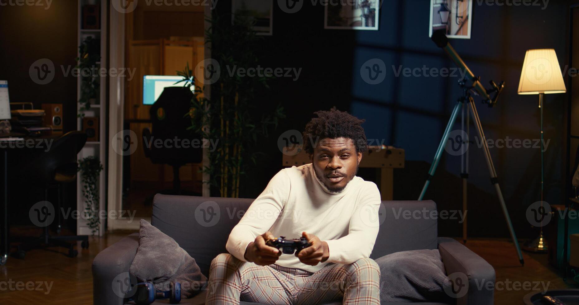 Man focused on playing singleplayer videogames on TV in cozy living room used as home theatre. African american gamer using controller to beat game on gaming console, relaxing on couch photo