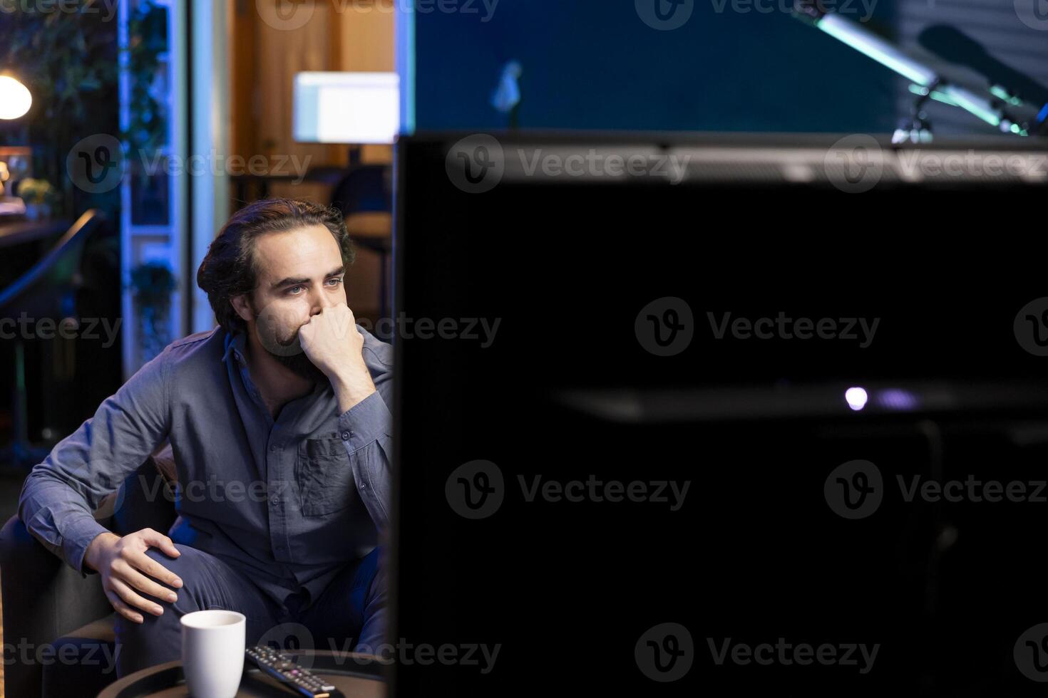 Person using TV to binge series on subscription based streaming services, enthralled by interesting movie. Man relaxing in apartment enjoying VOD shows on television display photo