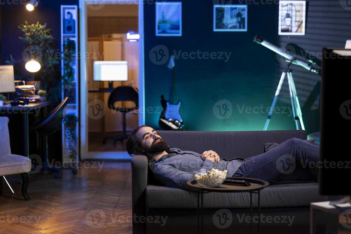 Smiling fan lounged on couch looking satisfied at favorite team winning while watching live sports event on TV. Supporter laying down at home, relaxing, pleased with victory in competition photo