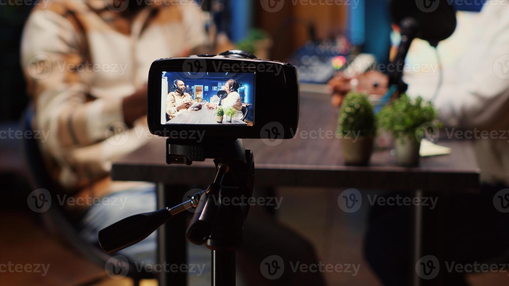 Focus on camera used by podcast host in blurry background to record guest telling interesting story to fans, panning shot. Close up of man and woman talking in studio, filmed by professional equipment photo