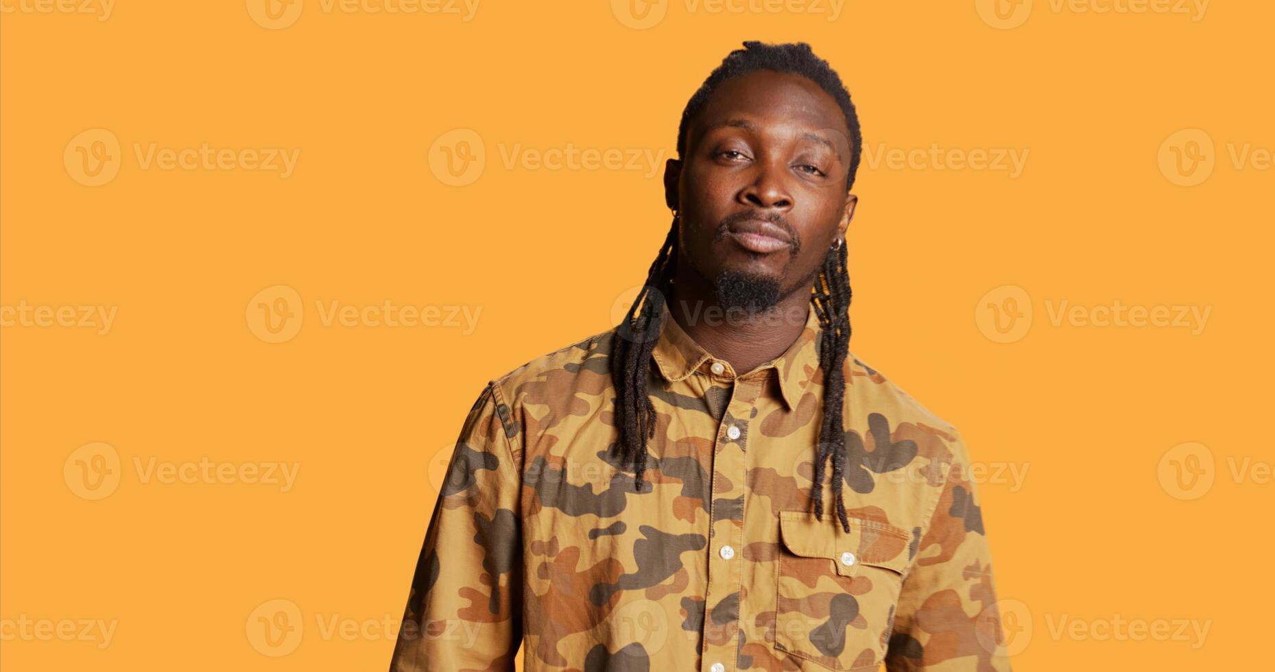 Male model feeling confident and smiling on camera, showing his relaxed cool walk over orange background. African american person with dreads posing in studio, stylish trendy guy. Handheld shot. photo