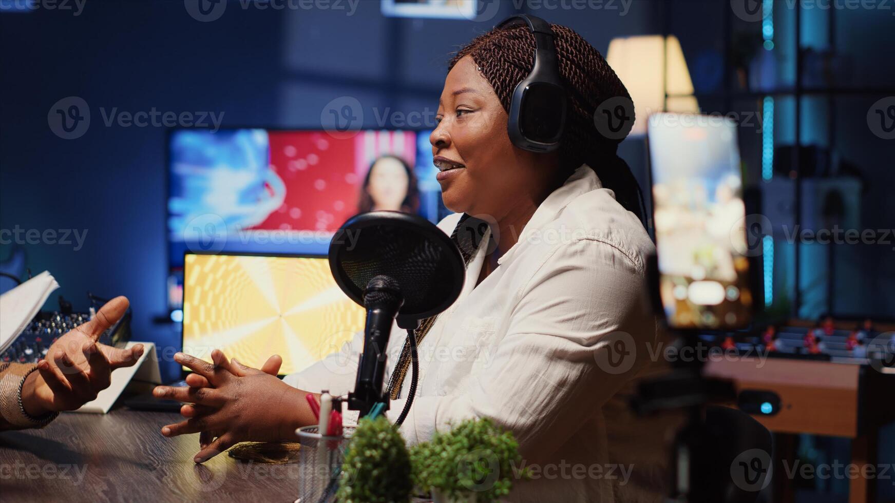 Journalist records interview with cellphone on tripod stabilizer in studio, reviewing notes to ask quality questions to guest. Close up of woman using phone to film vlog, talking on mic with celebrity photo