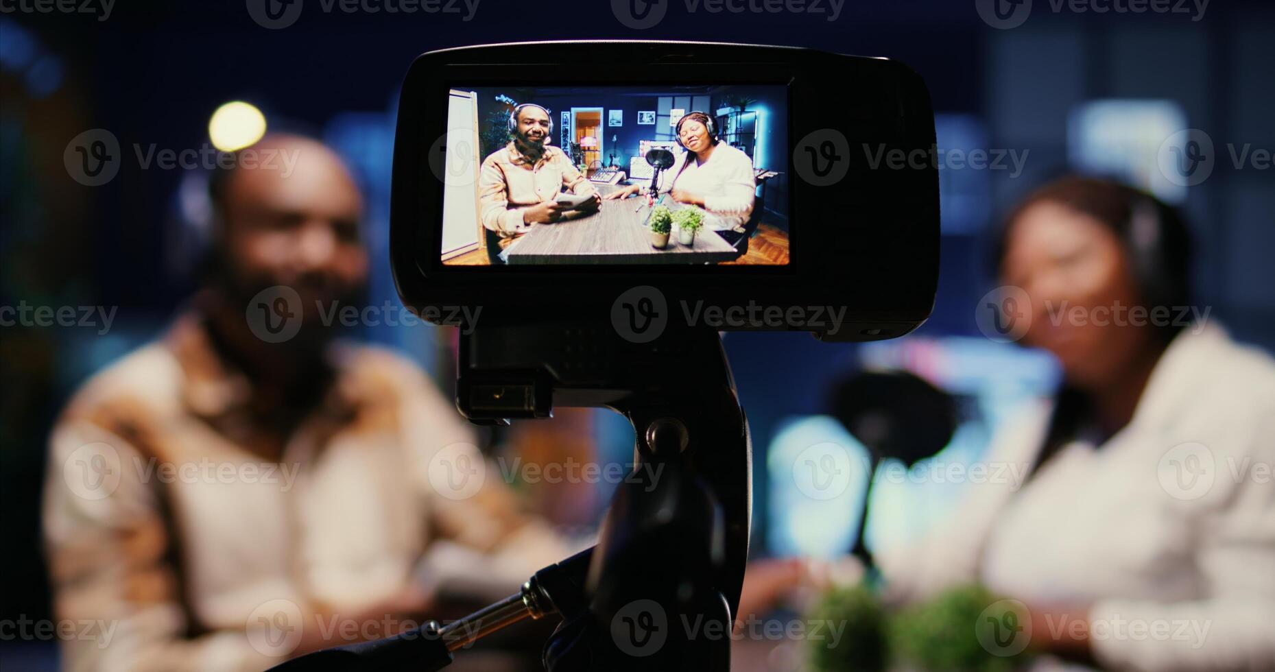 Focus on vlogging camera used by cohosts in blurry background streaming podcast during live debate on vlog channel. Close up of professional recording gear used by man and woman in studio to film show photo