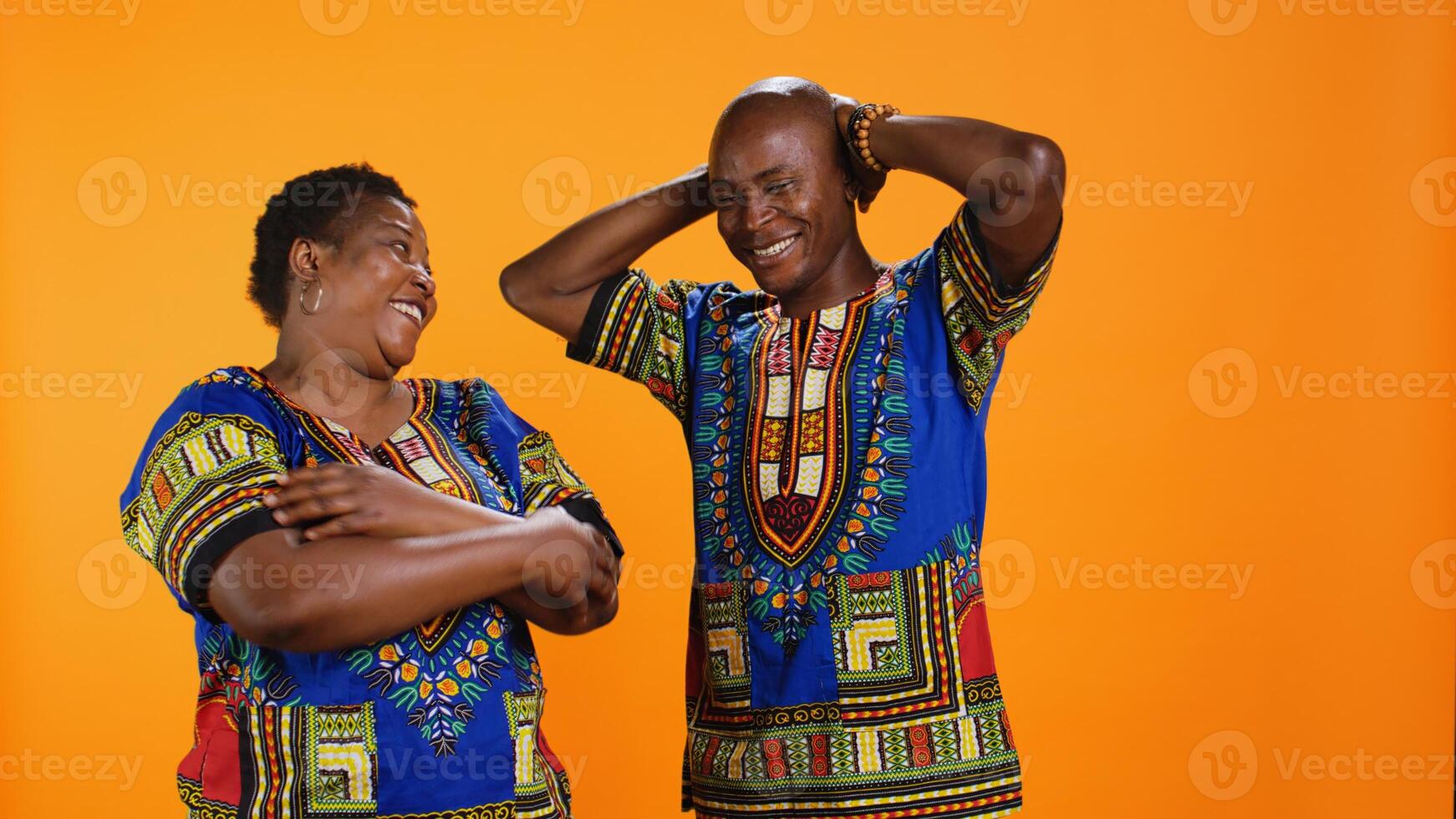 Cheerful husband and wife laughing together on camera, having fun with silly jokes over orange background. African american couple enjoying funny moments, carefree people laugh. photo
