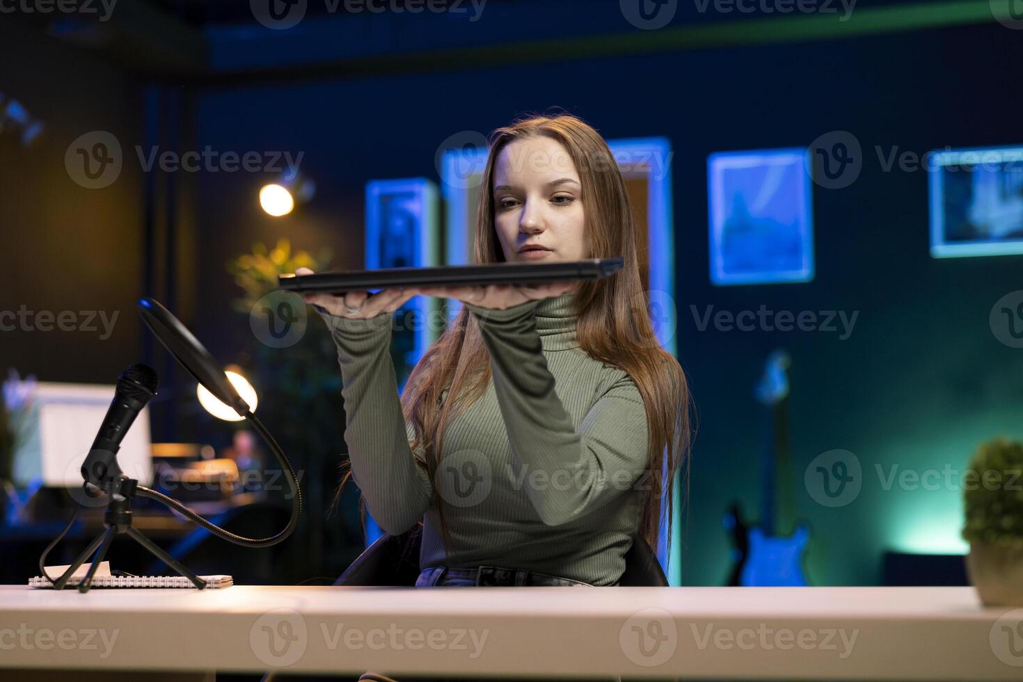 Young entertainer presenting laptop from brand sponsoring , urging viewers to purchase it. Girl does influencer marketing by advertising digital device to audience in studio photo