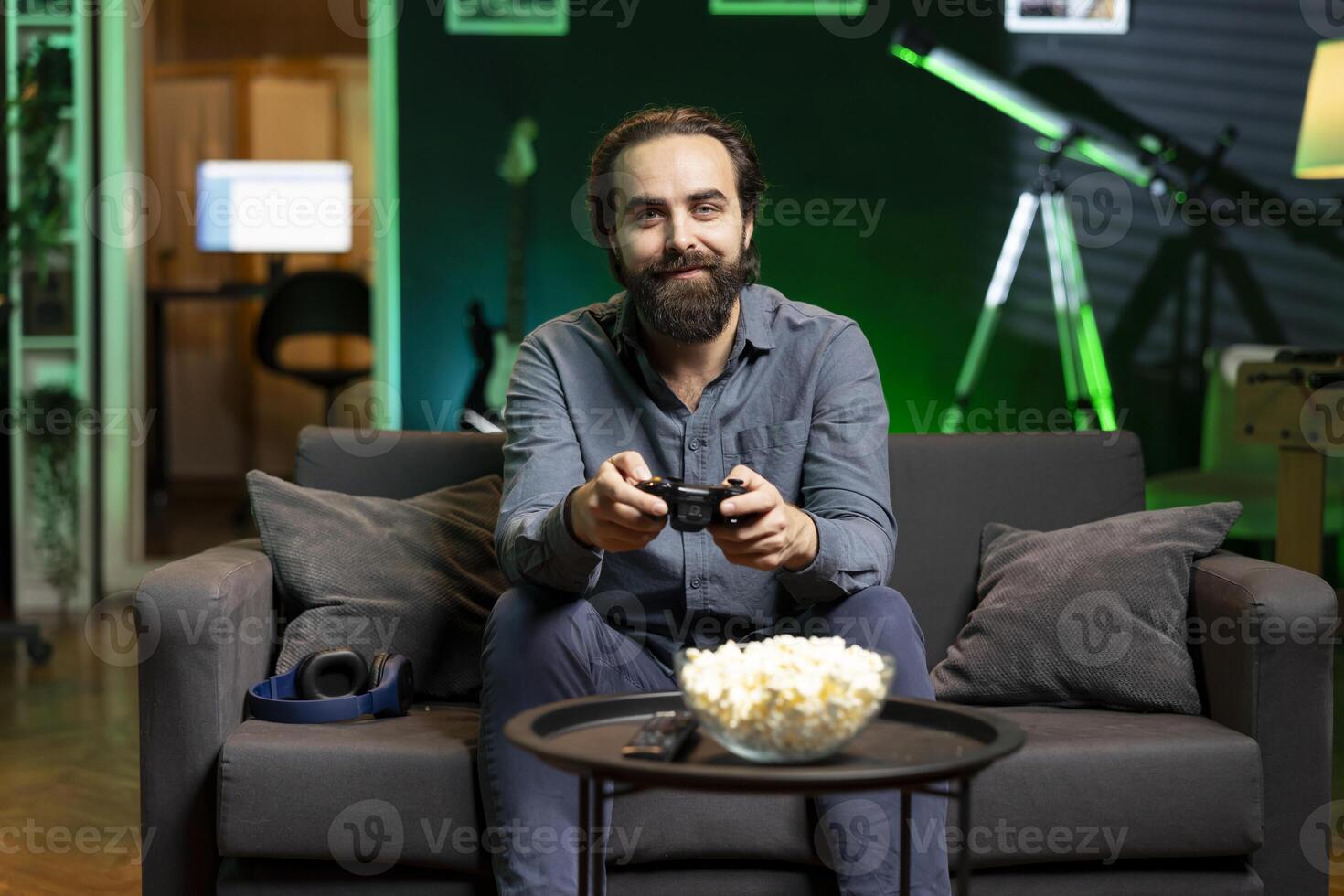 Gamer immersed in virtual world, eating popcorn in modern apartment and playing videogames. Jolly man enjoying snacks during gaming session from the comfort of his living room photo