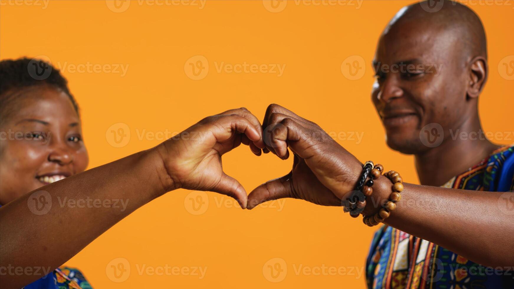Ethnic couple in love showing heart shape sign and kissing in front of camera, sharing their affection and sincere feelings. Romantic people share kiss in studio, presenting love symbol. Close up. photo