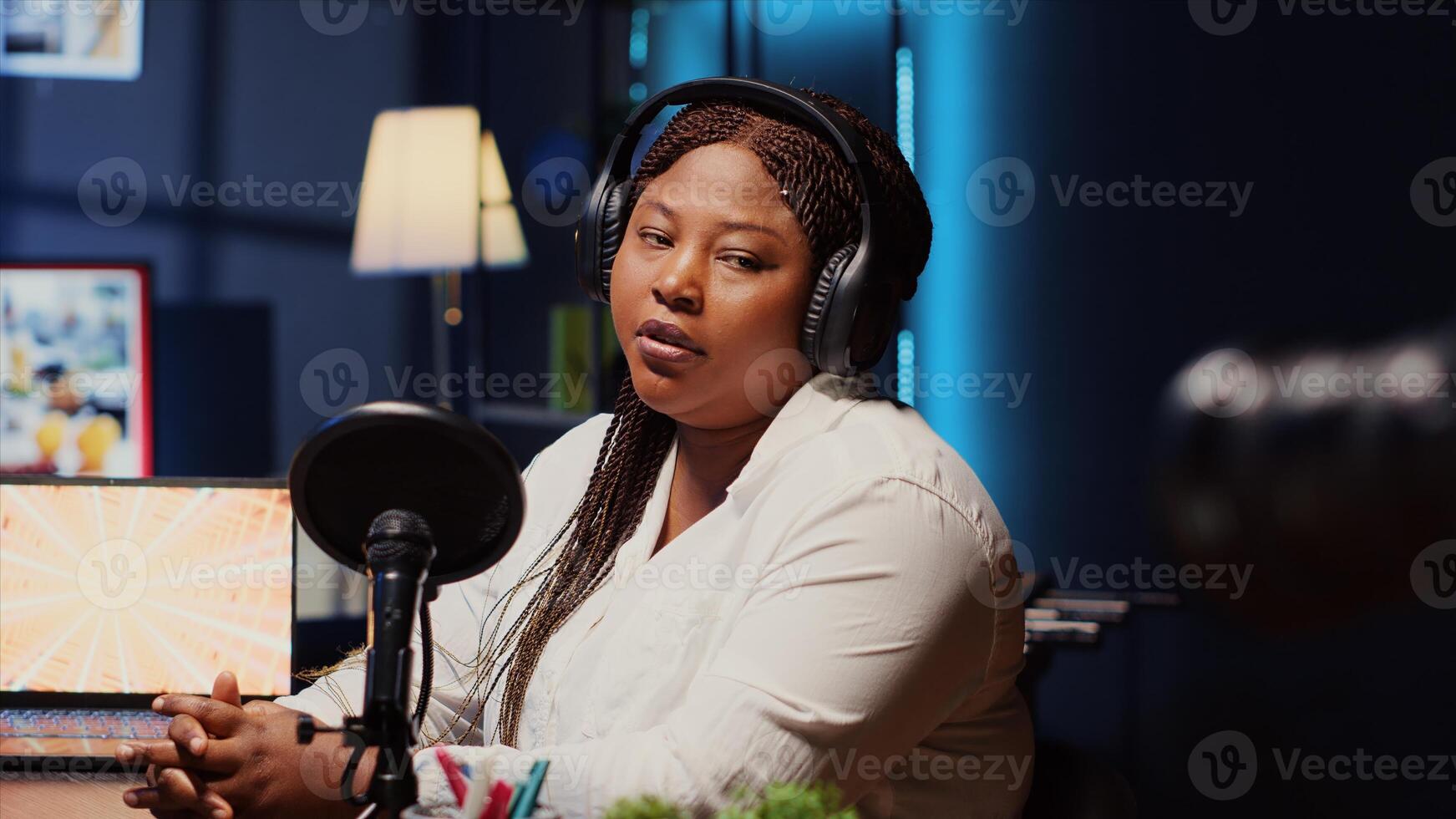 Woman hosting podcast, saluting audience while recording entertaining discussion in apartment studio. Happy presenter uses professional camera to produce comedy internet show, greeting viewers photo