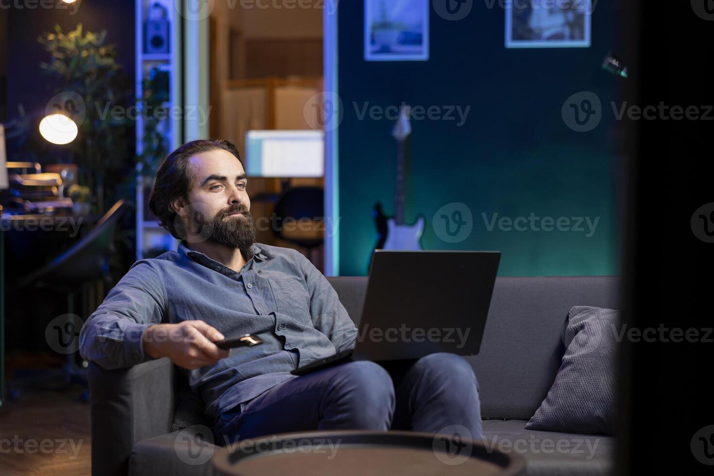 Man watching interesting movie on streaming service with laptop on lap, enjoying time off from work. Person on couch consuming snacks, looking at films broadcasted on TV and holding notebook photo