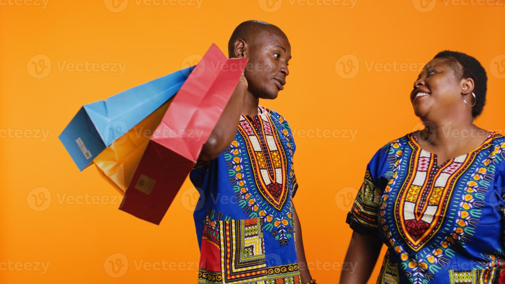 Tired man carrying shopping paper bags for his jolly wife, taking her to the store during sale season. Smiling woman having fun with bargain commerce while her husband is suffering at mall. photo