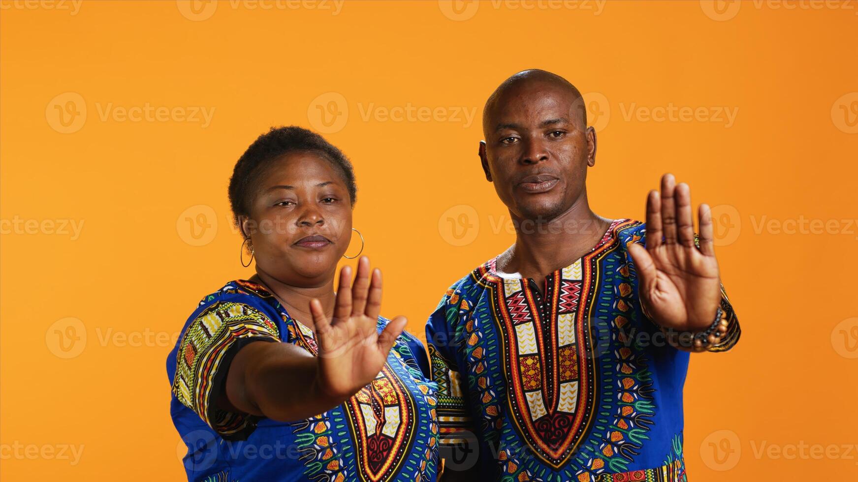 African american couple doing stop symbol with palm, expressing negativity and indicating refuse over orange background. Ethnic married people being displeased with something, warning sign. photo