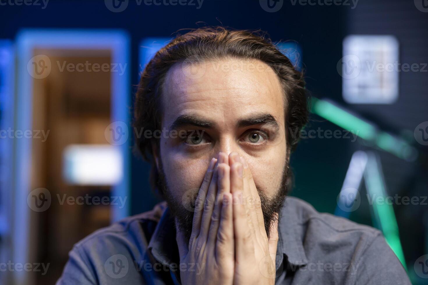 Portrait of cord cutter covering mouth in shock while looking in disbelief at TV displaying thriller film. Disturbed person at home watching movie on on demand channel, stupefied by plot twist photo