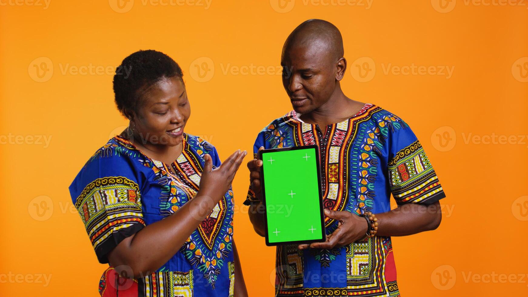 African american married couple holding tablet with greenscreen, pointing at isolated chromakey display on mobile device. Man and woman looking at gadget layout with blank copyspace screen. photo