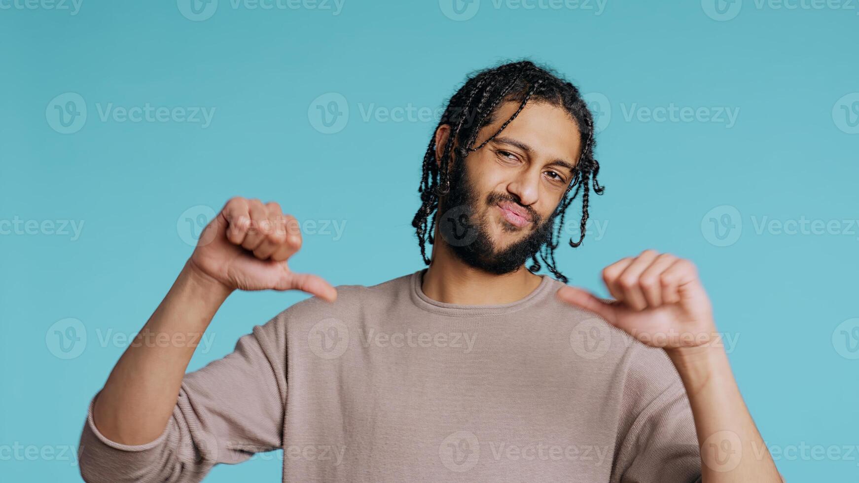 Upset Middle Eastern man showing thumbs down sign gesturing, disapproving, offering negative feedback. Disappointed BIPOC person doing rejection hand gesture, studio background, camera B photo