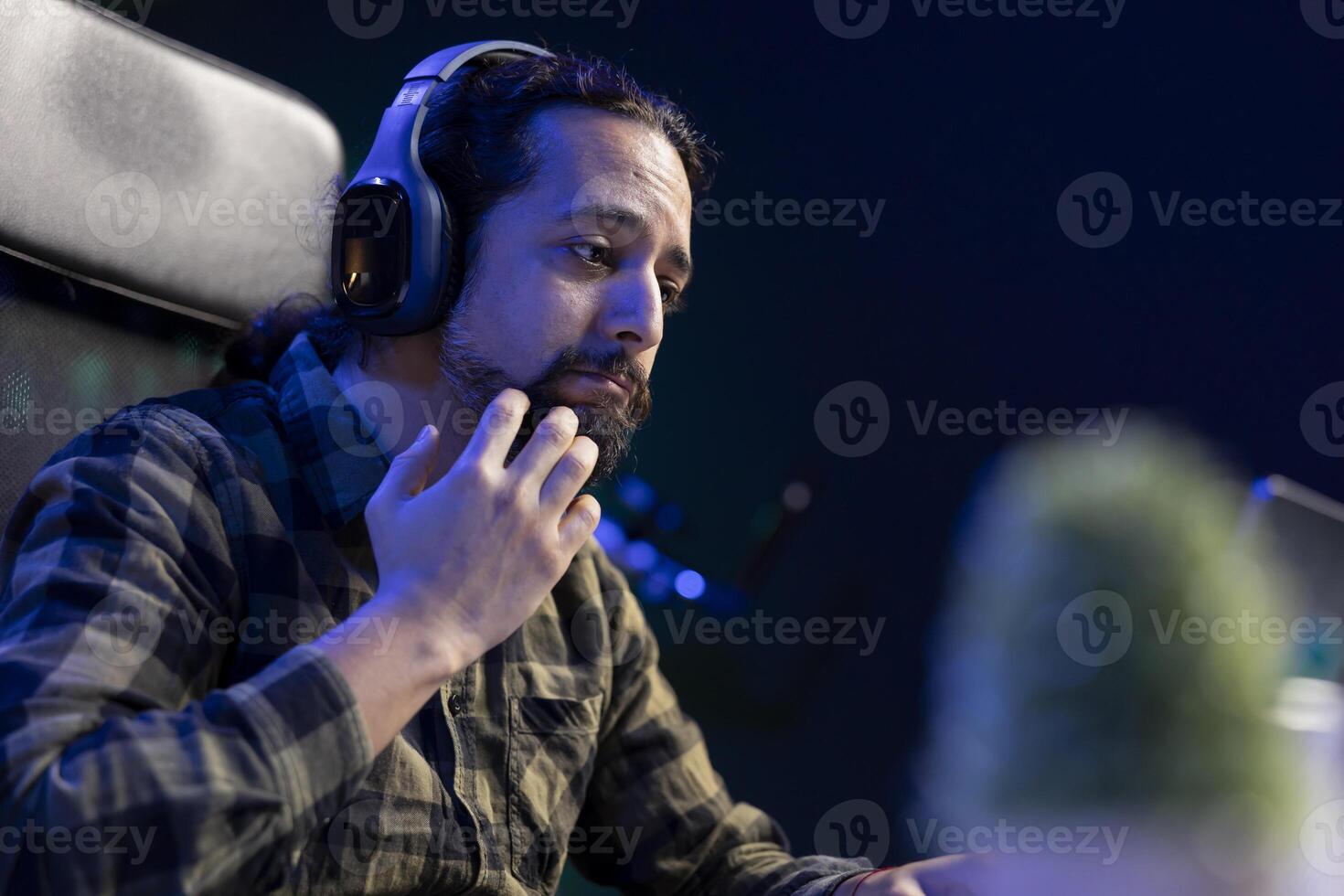 Male student surfing the net and listening to music with wireless headphones and laptop. Man with his hand on chin is wearing headset is having a conference on portable computer at home. photo