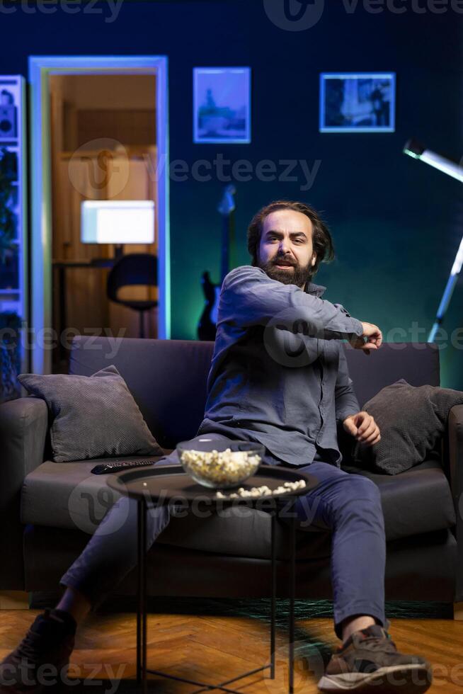 Sports fan watching football competition live on TV, reacting in anger to goal scored by opposing team. Supporter at home annoyed by refereeing mistake sending favorite player off the field photo