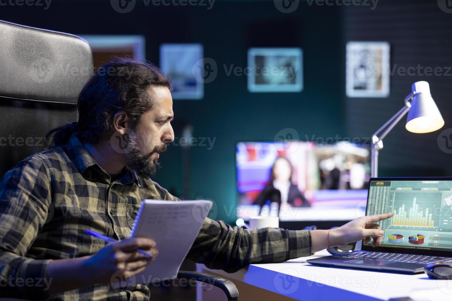 Dedicated man utilizing a laptop and pen at his desk, conducting financial research, and coming up with ideas. Male, focused, and productive, uses technology and a notebook for work and study. photo