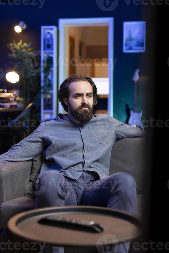 Man watching depressing movie broadcasted on TV, saddened by main character dying at the end. Upset person with teary eyes on couch affected by troubling events in film scene photo