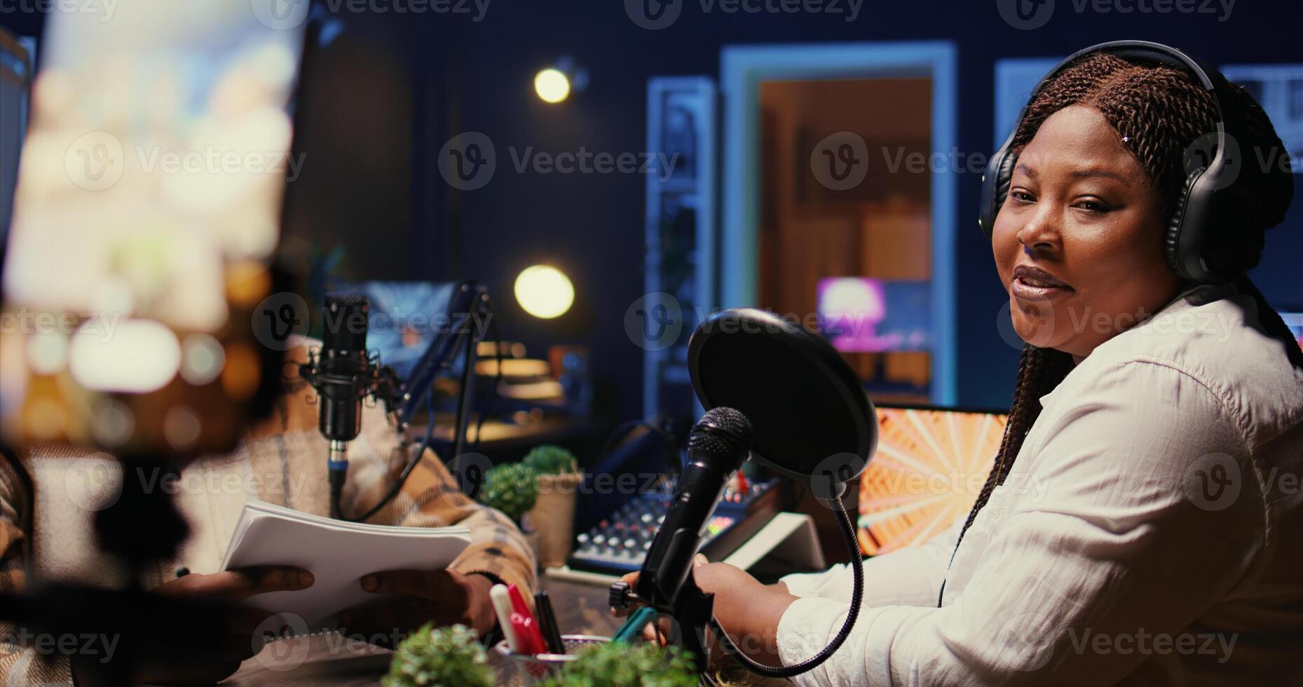 Woman laughing during comedy focused podcast filmed with cellphone on tripod stabilizer. Guest amused by talking show host telling jokes, recording with phone, handheld camera shot photo