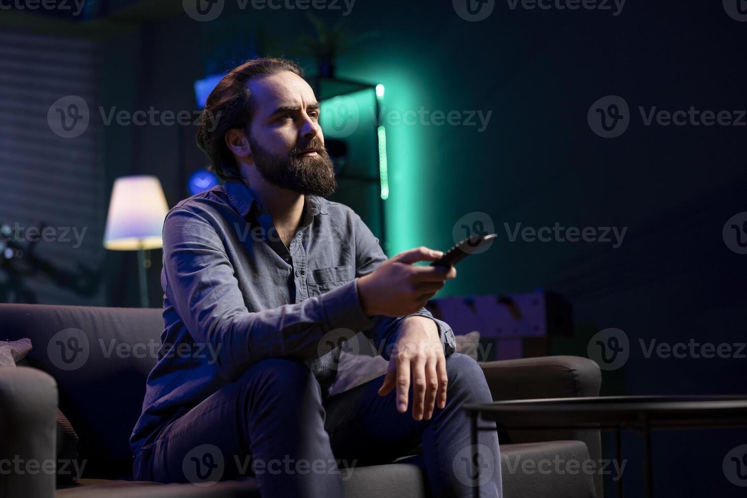 Man using remote control to switch channels, gripped by suspenseful films shown on television screen. Person mindlessly scrolling through streaming content, stopping after seeing interesting movie photo
