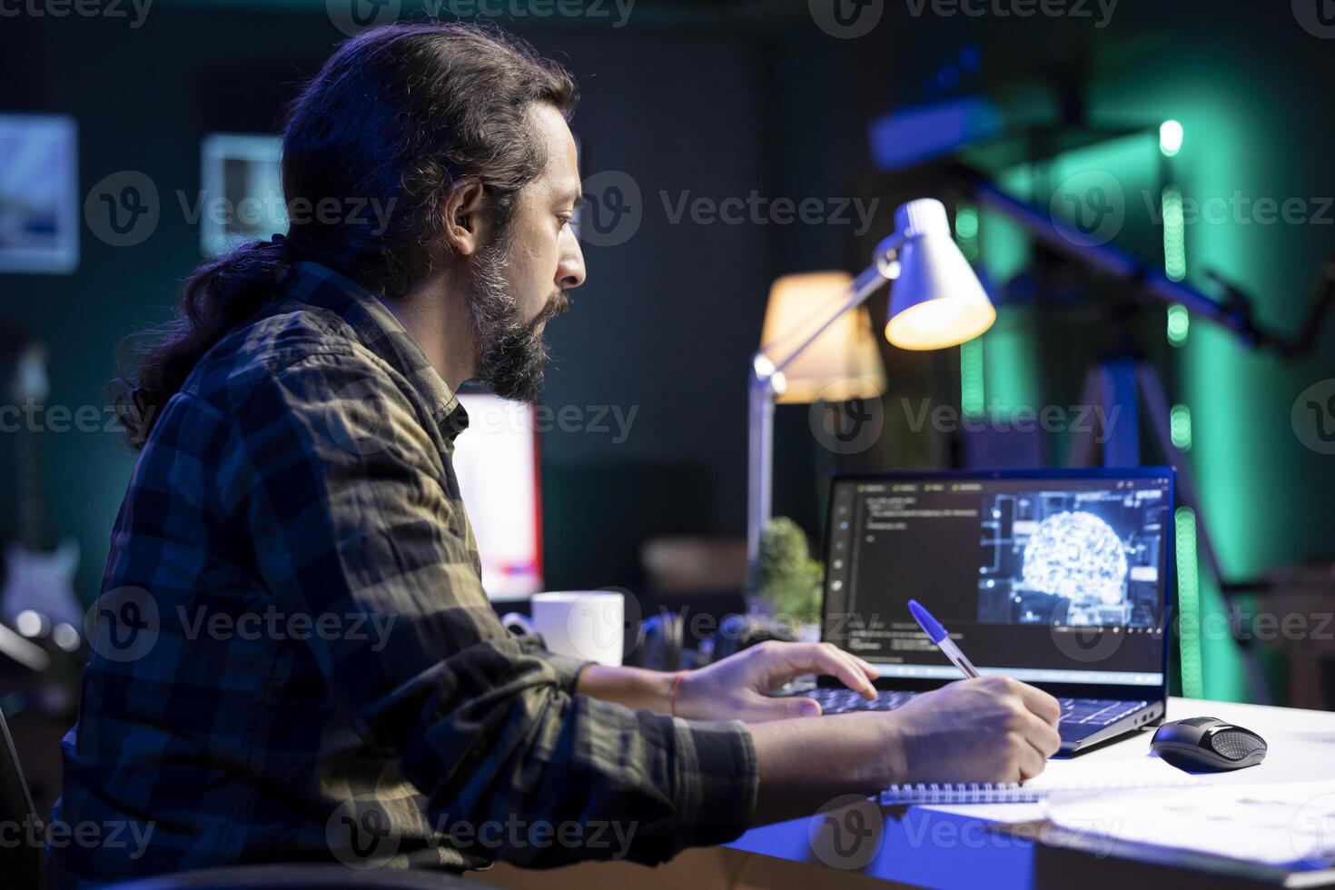 Man at desk using laptop for programming and data analysis. Male programmer working at home, using his notepad while efficiently managing information technology and data center on digital device. photo