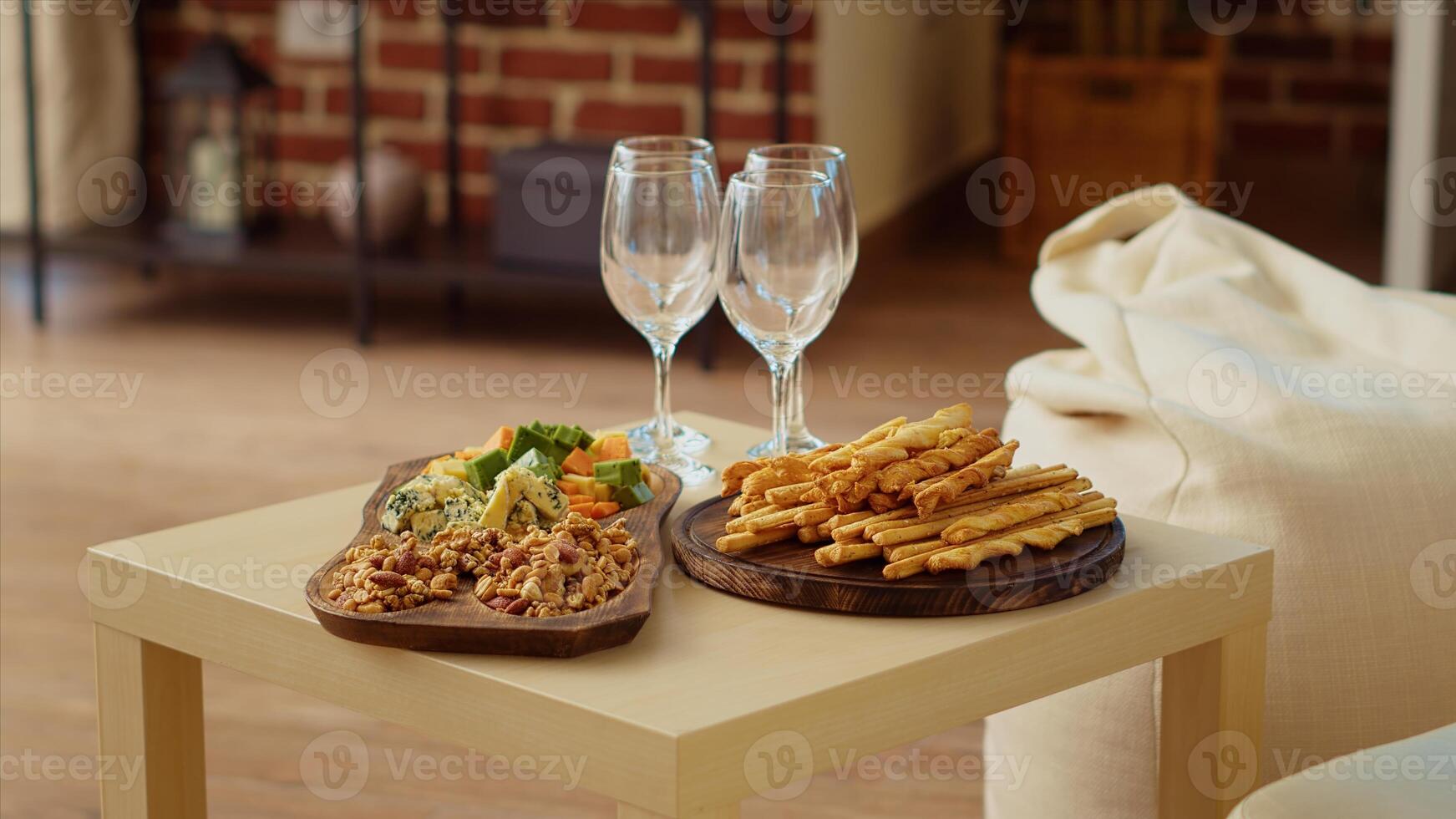 Charcuterie board and gourmet cheese platter set up by hosts to properly welcome guests arriving soon at apartment party. Wine glasses next to snacks in brick wall living room photo