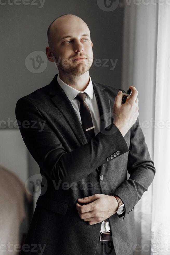 A man in a suit and tie is getting ready to spray cologne. The image has a professional and polished feel, with the man standing in front of a window photo