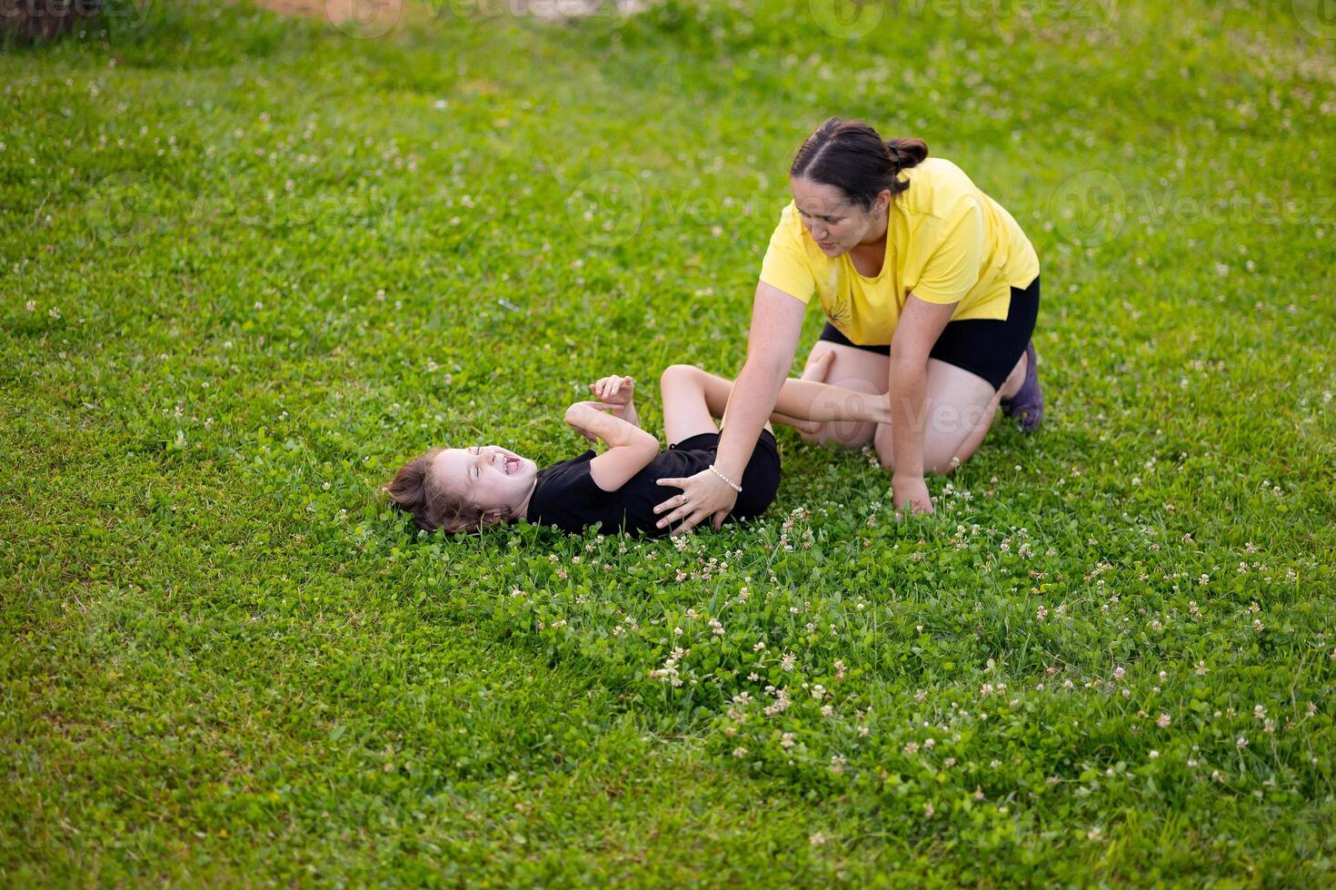 young mother and daughter are playing on the green lawn and laughing happily. Mutual understanding between daughter and child, trust, caring for children, happy motherhood, wise mother. photo