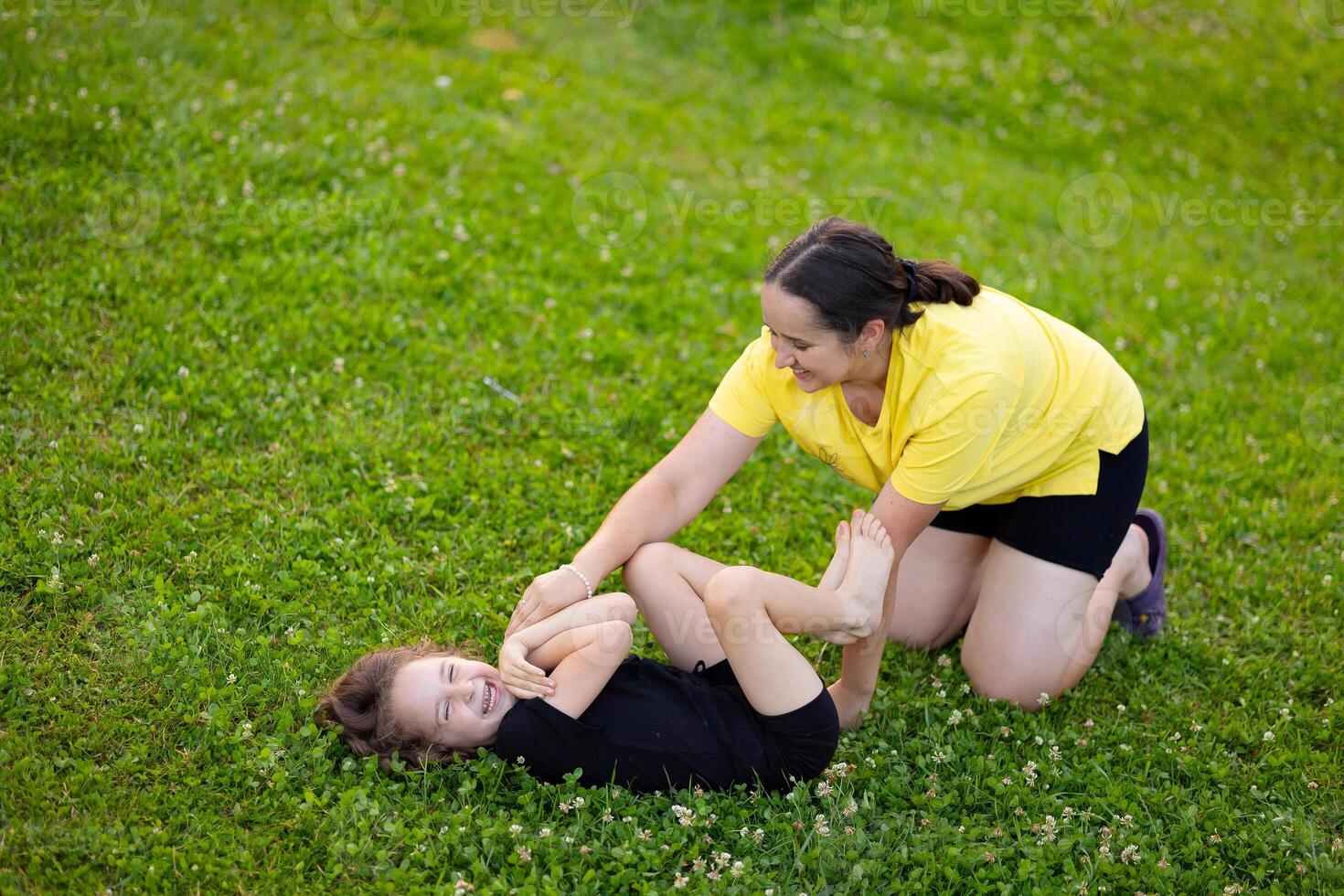 young mother and daughter are playing on the green lawn and laughing happily. Mutual understanding between daughter and child, trust, caring for children, happy motherhood, wise mother. photo