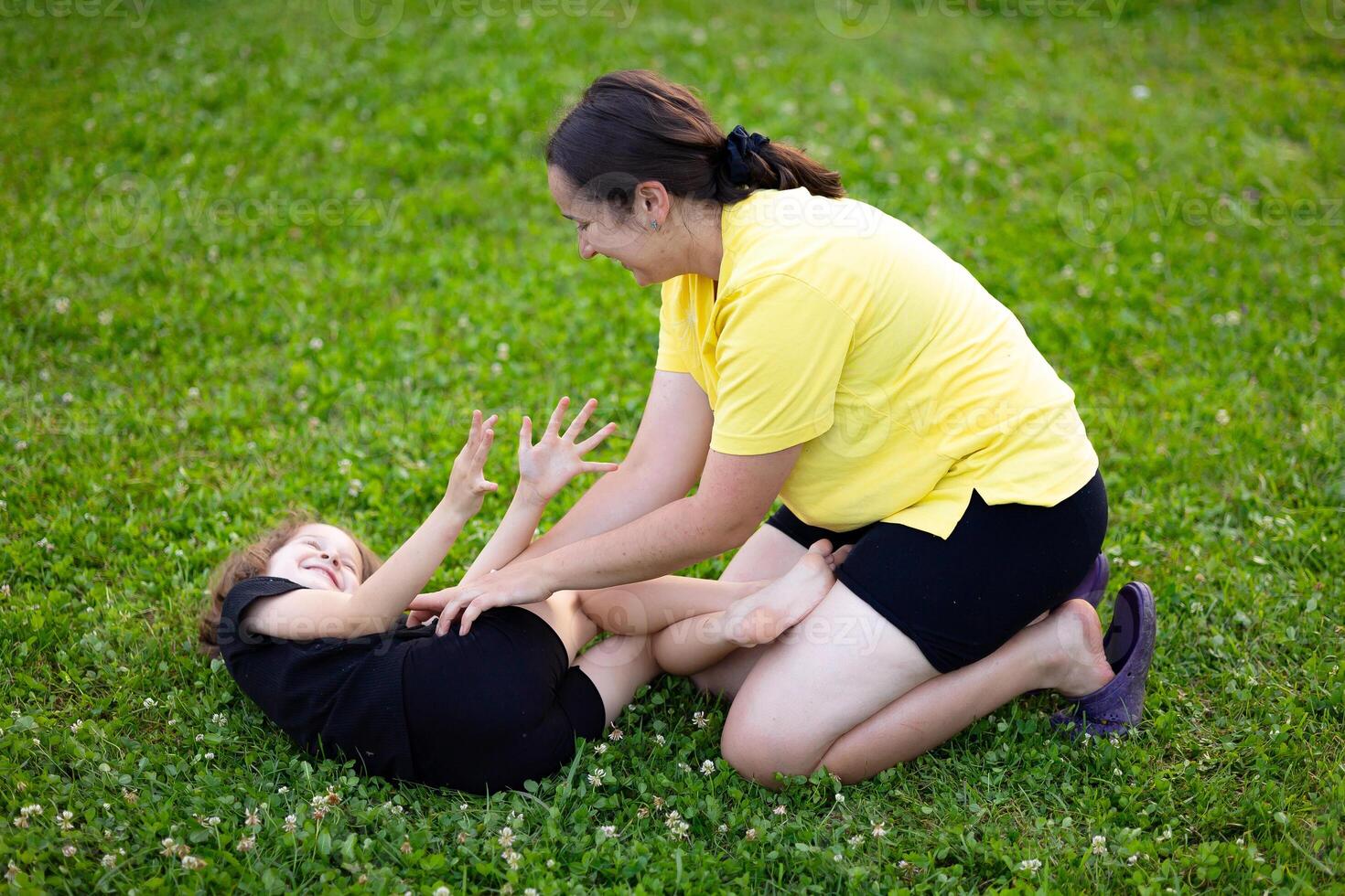 young mother and daughter are playing on the green lawn and laughing happily. Mutual understanding between daughter and child, trust, caring for children, happy motherhood, wise mother. photo