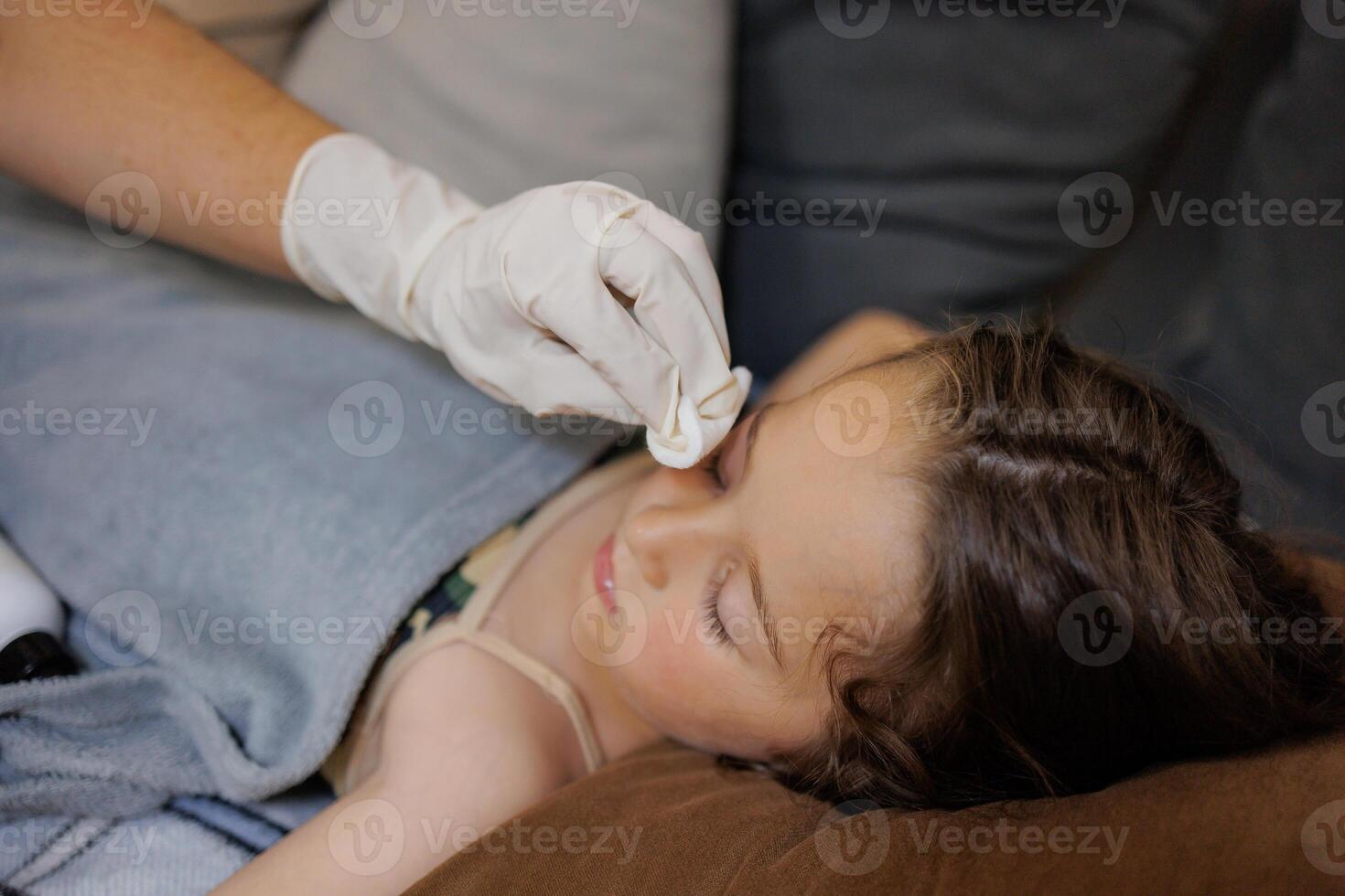 a small childhood infection on the eyelid caused by insect, mosquito or bee bites that causes swelling, redness, heat and itching. A mother is trying to remove swelling from a child's eye photo