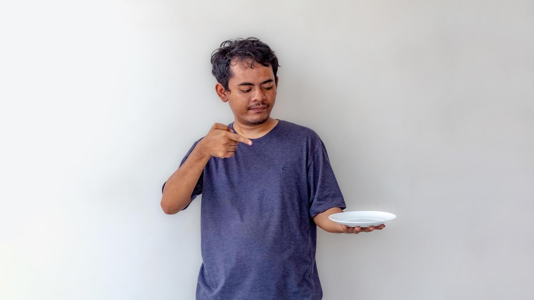 Adult man holding an empty white plate while pointing at it, as if presenting food, isolated on a white background. Perfect for themes related to cooking, food presentation, or meal preparation. photo