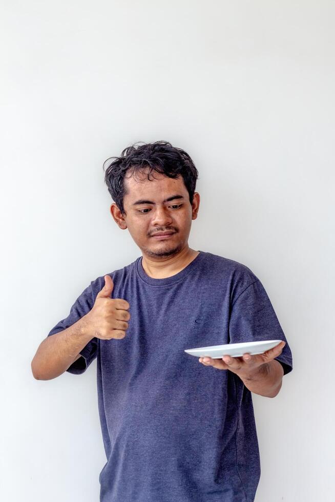 Adult man holding an empty white plate while giving a thumbs up and smiling, isolated on white background. Perfect for themes related to cooking, food presentation, and positive emotions. photo