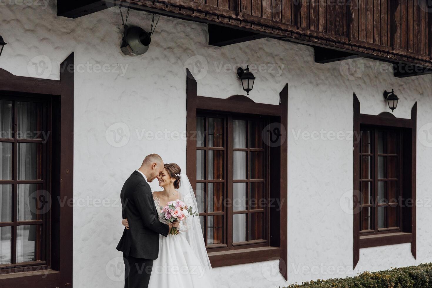 A bride and groom are standing in front of a building, with the bride holding a bouquet photo