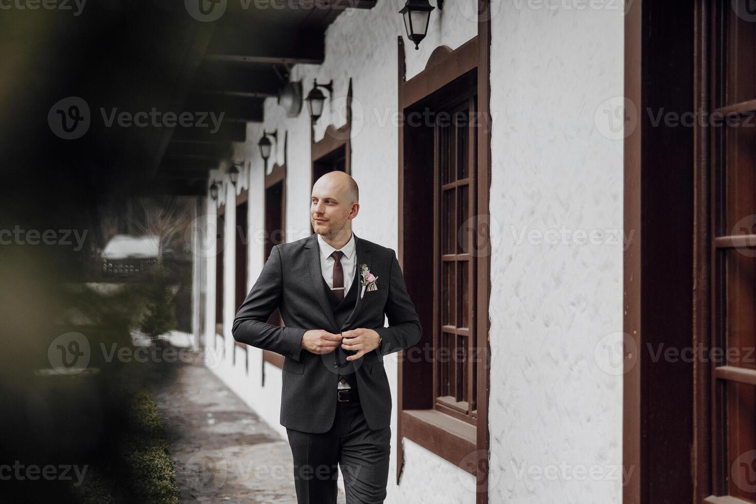 A man in a suit is standing in front of a building, adjusting his tie. Concept of formality and professionalism, as the man is dressed in a suit and tie photo