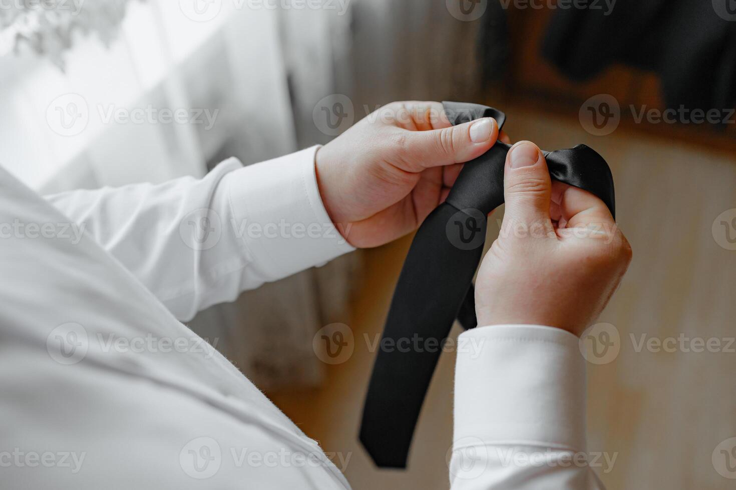 A man is holding a black tie and adjusting it. Concept of formality and attention to detail, as the man is carefully adjusting his tie to ensure it is properly aligned photo