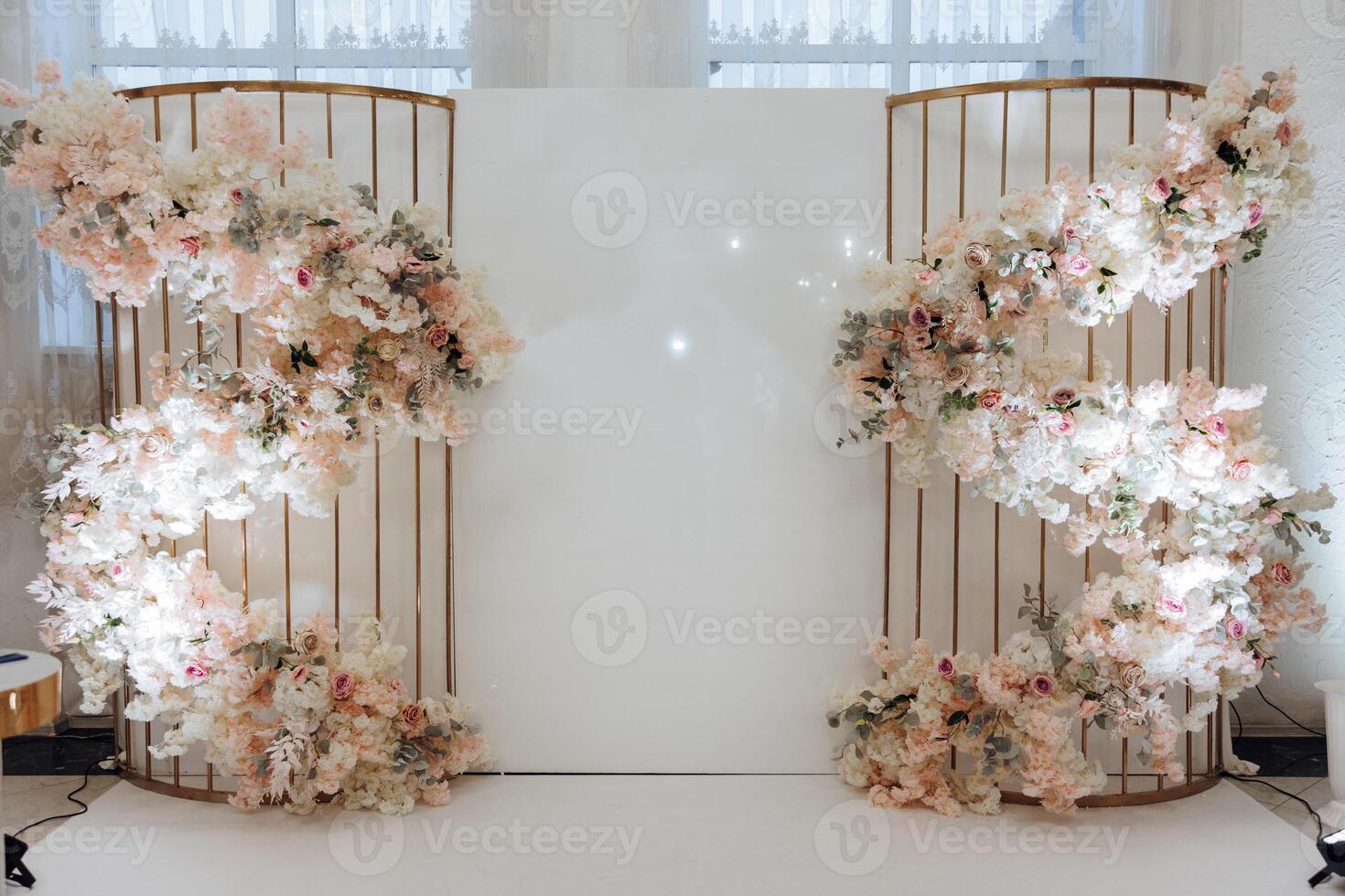 A large white wall with a floral arrangement on it. The arrangement is made up of pink and white flowers, and it is surrounded by a metal frame. The flowers are arranged in a spiral pattern photo