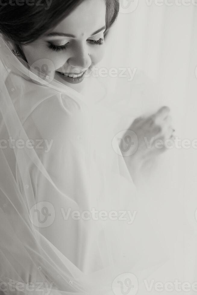 A bride is posing for a picture with her veil pulled back. She is smiling and looking at the camera photo