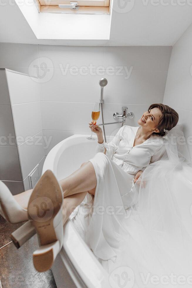 A woman in a white dress is sitting in a bathtub with a glass of wine. Concept of relaxation and indulgence, as the woman enjoys her time in the bathtub while sipping on her drink photo