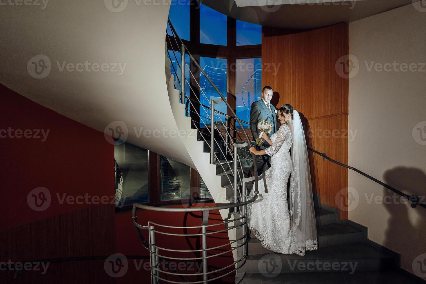 A bride and groom are standing on a spiral staircase, with the bride holding a bouquet. Concept of romance and celebration, as the couple is getting ready to start their new life together photo