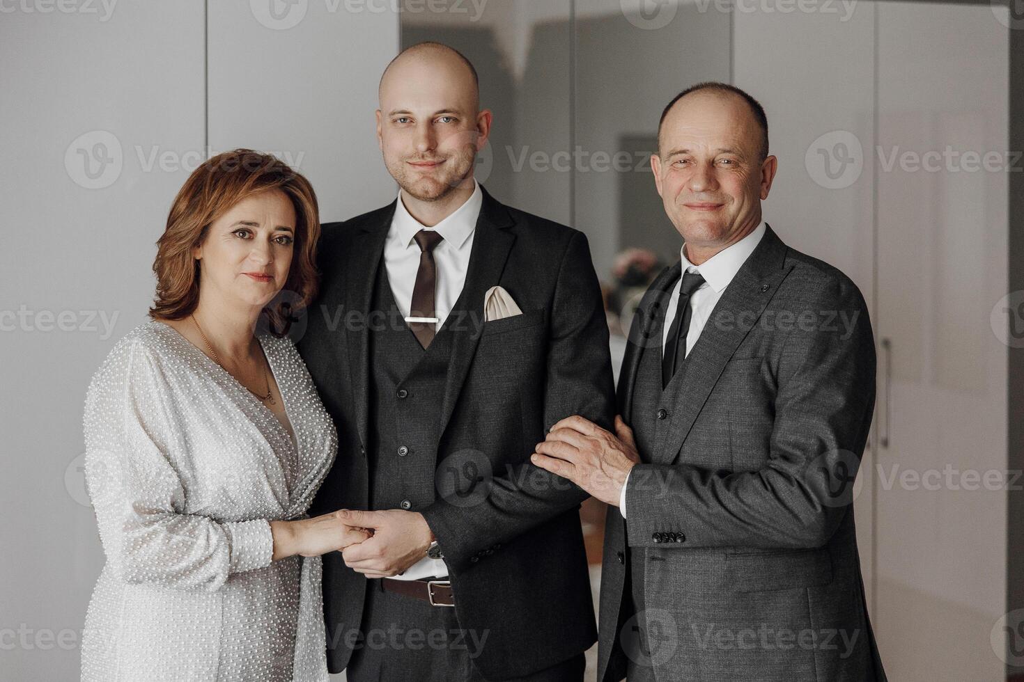 A man and two women are posing for a picture. The man is wearing a suit and tie, and the woman is wearing a dress. Scene is formal and elegant photo