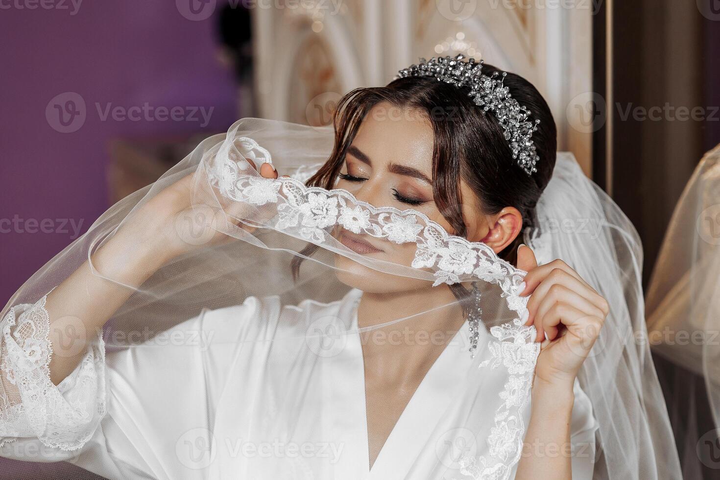A woman is getting ready for her wedding and is putting on a veil. She is wearing a white dress and a white veil photo