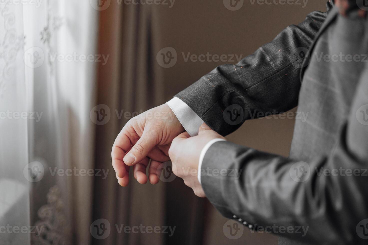 A man is getting dressed in a suit and tie. He is adjusting his tie and putting on his cuff photo