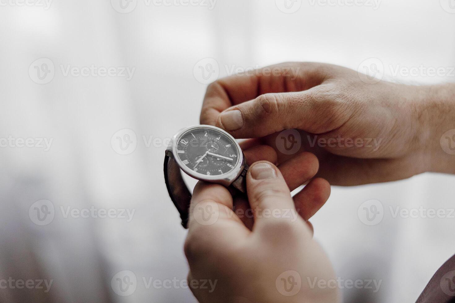 A man is holding a watch in his hand. The watch is black and silver. The man is looking at the watch, possibly checking the time photo
