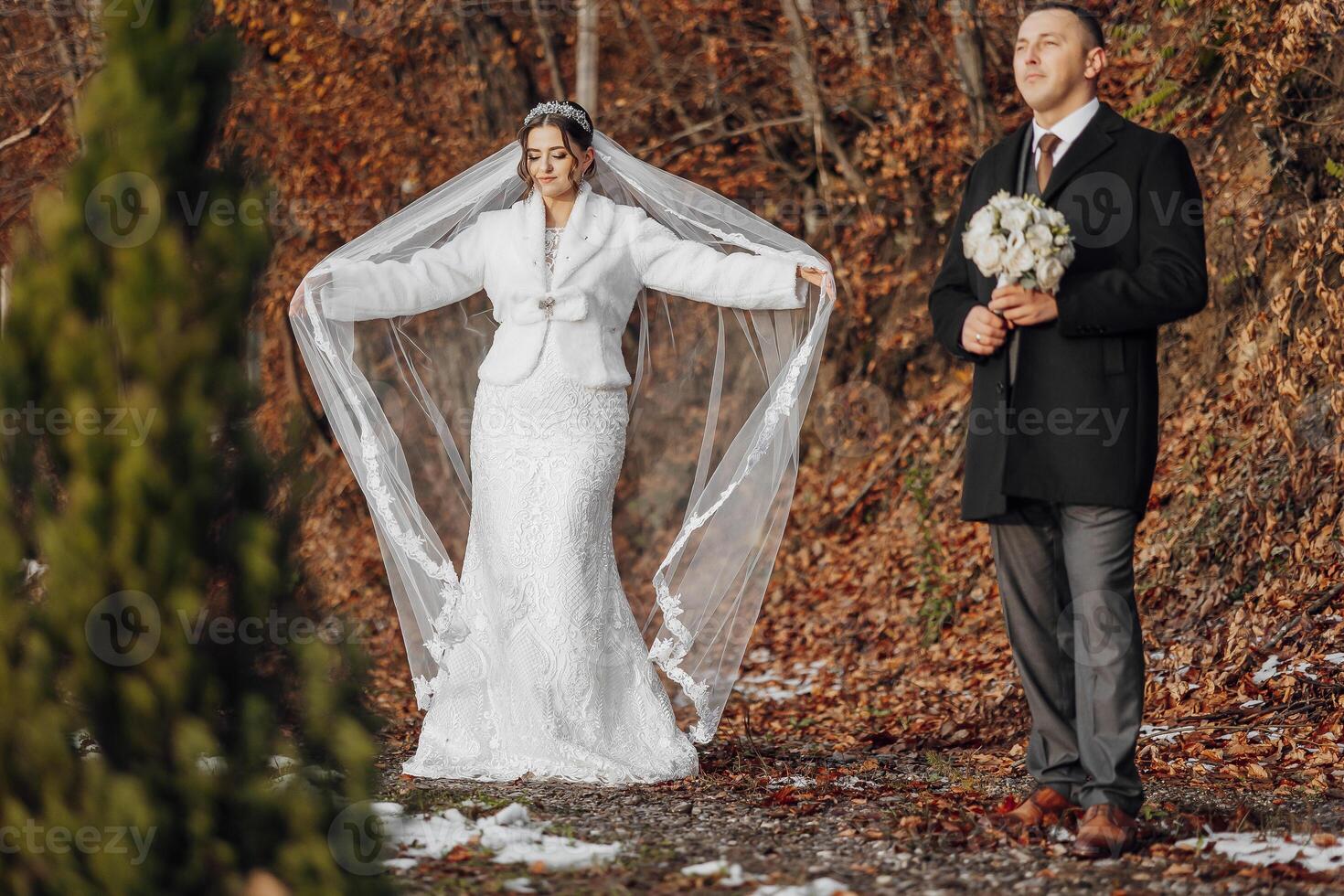 A bride and groom stand in a forest, the bride holding a bouquet. Scene is romantic and serene photo