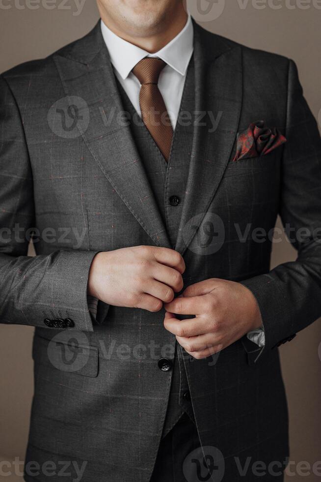A man in a suit is wearing a red rose tie and a red rose pocket square. He is adjusting his tie and jacket, giving the impression of a formal event photo